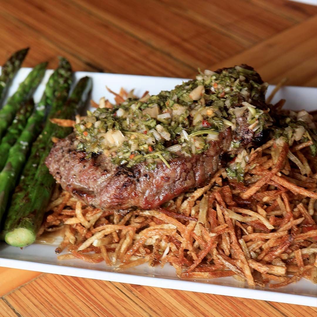 A plate of premium steak frites topped with fresh house-made chimichurri and served with a side of crispy golden fries at The Back 40.