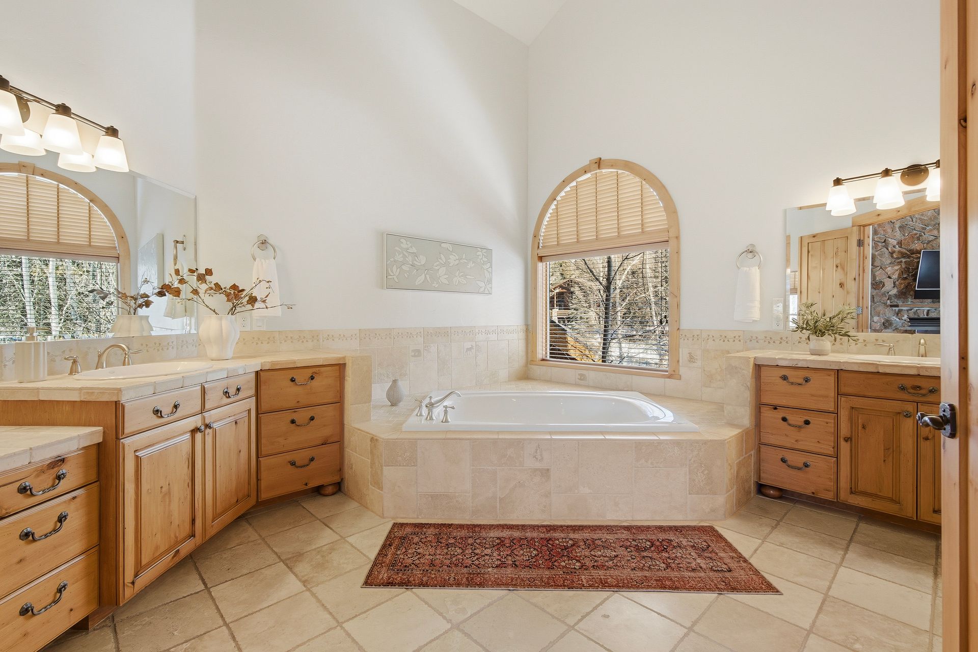 Spa-inspired primary bathroom with dual natural stone vanities and a deep jetted soaking tub.
