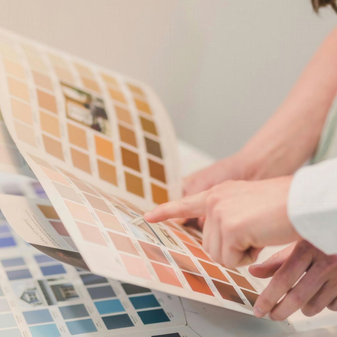 Two hands holding and comparing several different paint swatches over a table, representing the interior design and finish selection process for a custom home build.