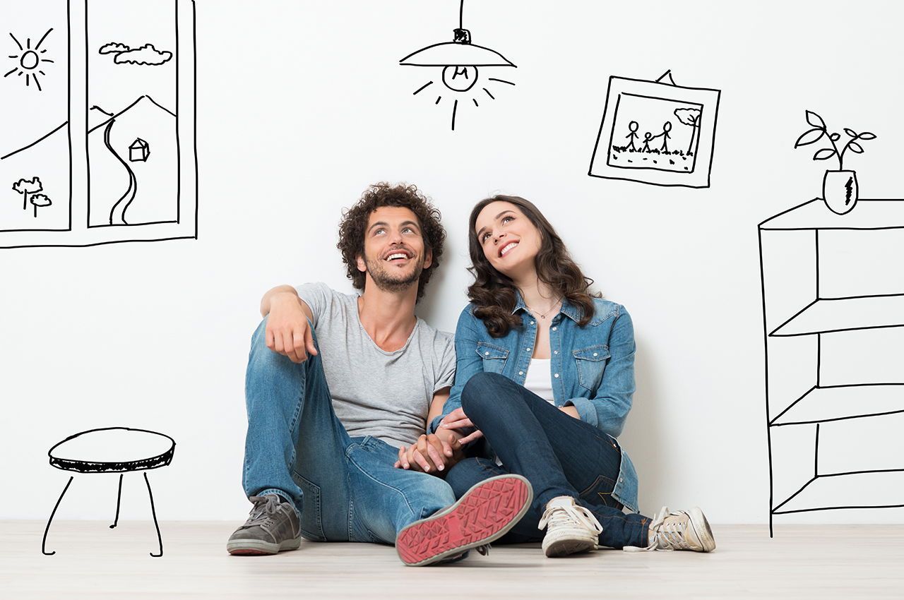 A man and a woman are sitting on the floor in front of a wall with drawings on it.