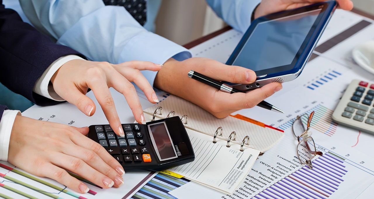 A group of people are sitting at a table using a calculator and a tablet.