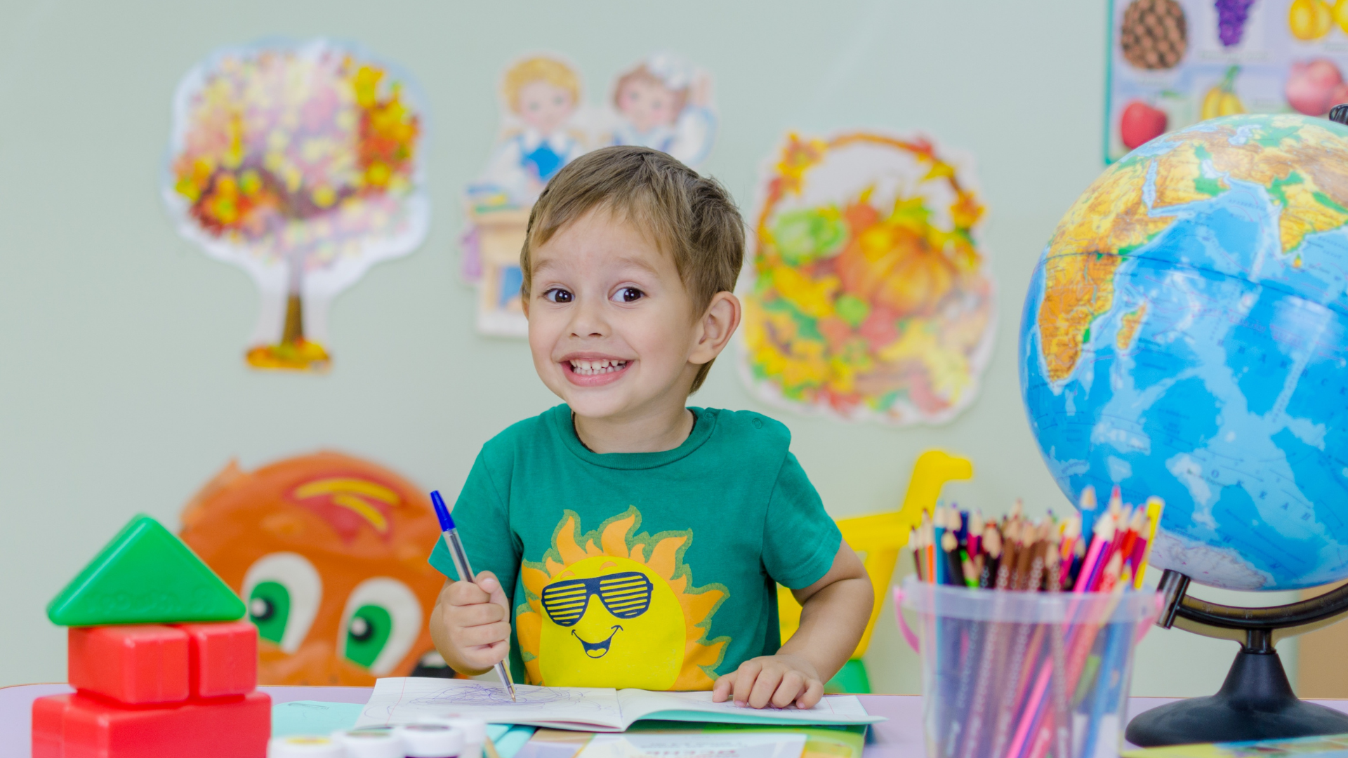 A young boy is sitting at a table in a classroom with a globe.
