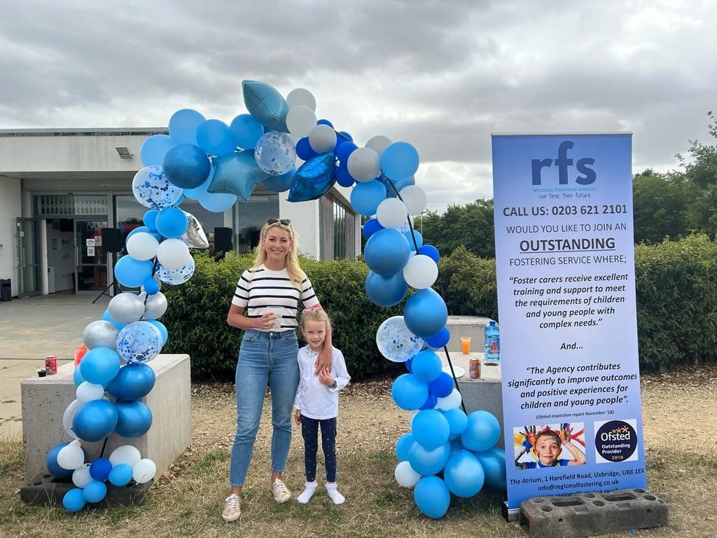 A woman and a child are standing under a blue and white balloon arch.