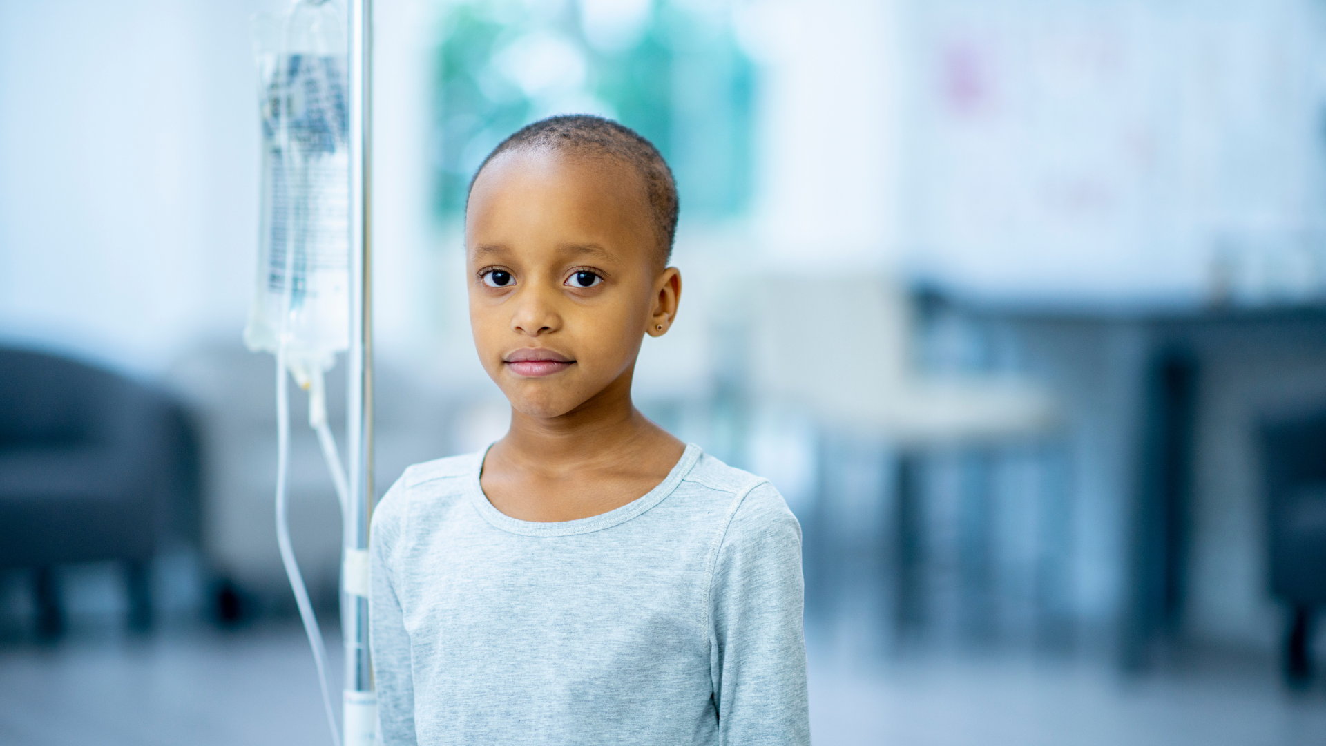 A young girl is standing in front of an iv in a hospital room.