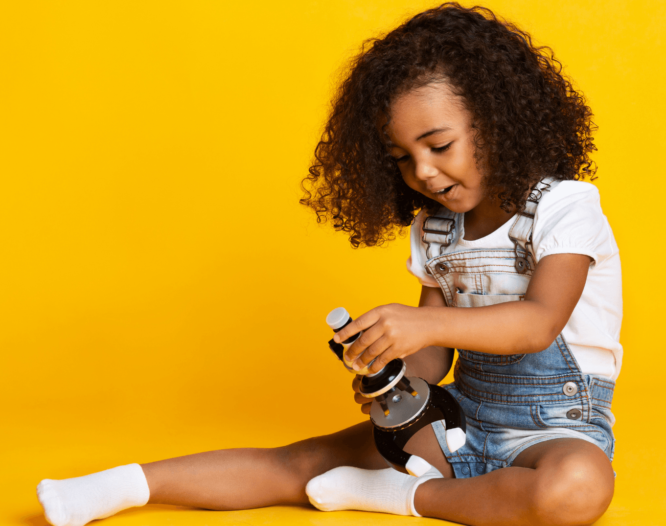 A little girl is sitting on the floor looking through a microscope.