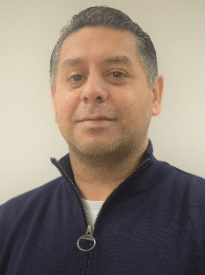Man with short dark hair in blue zip-up sweater, looking at the camera.