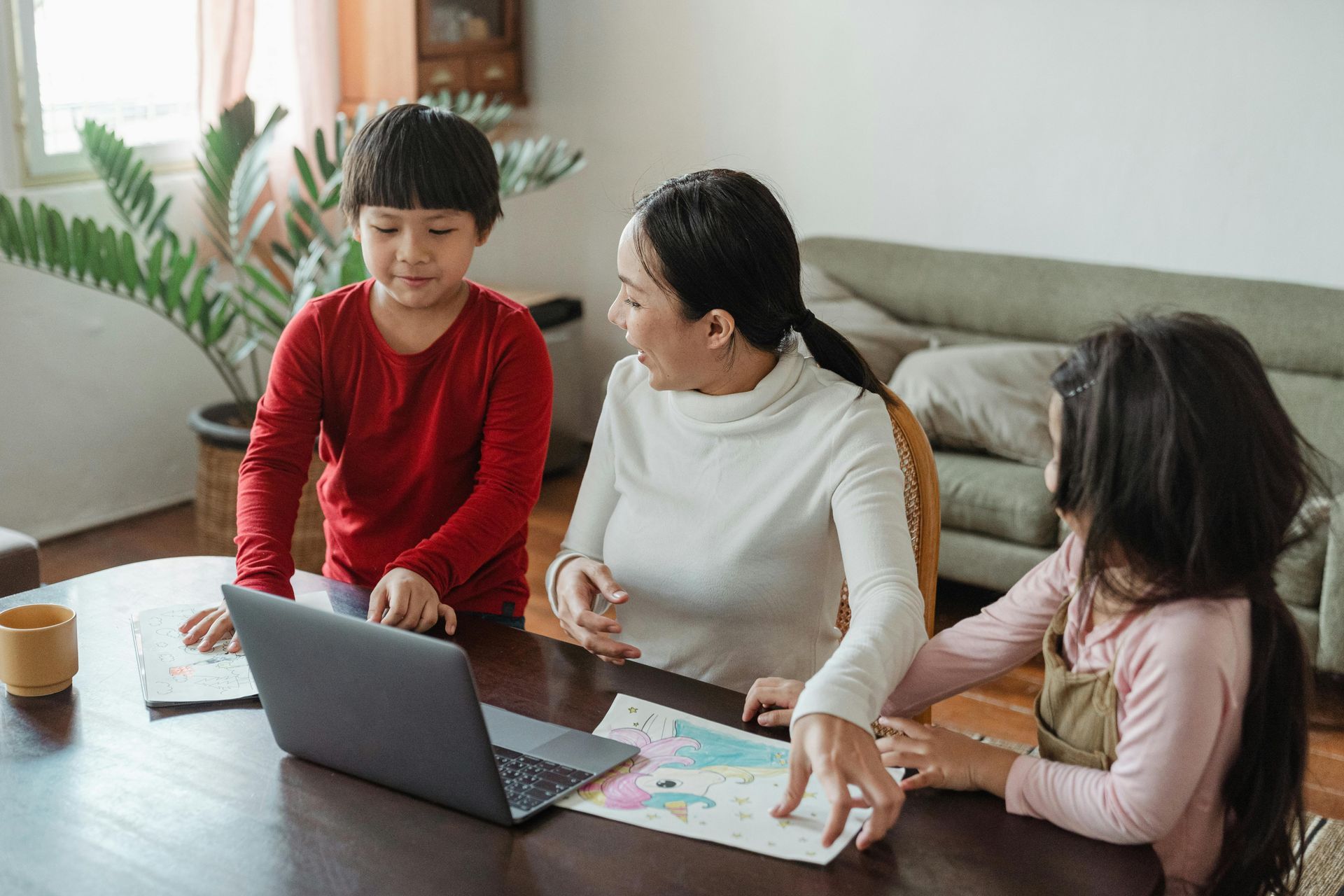 A woman and two children are sitting at a table looking at a laptop.