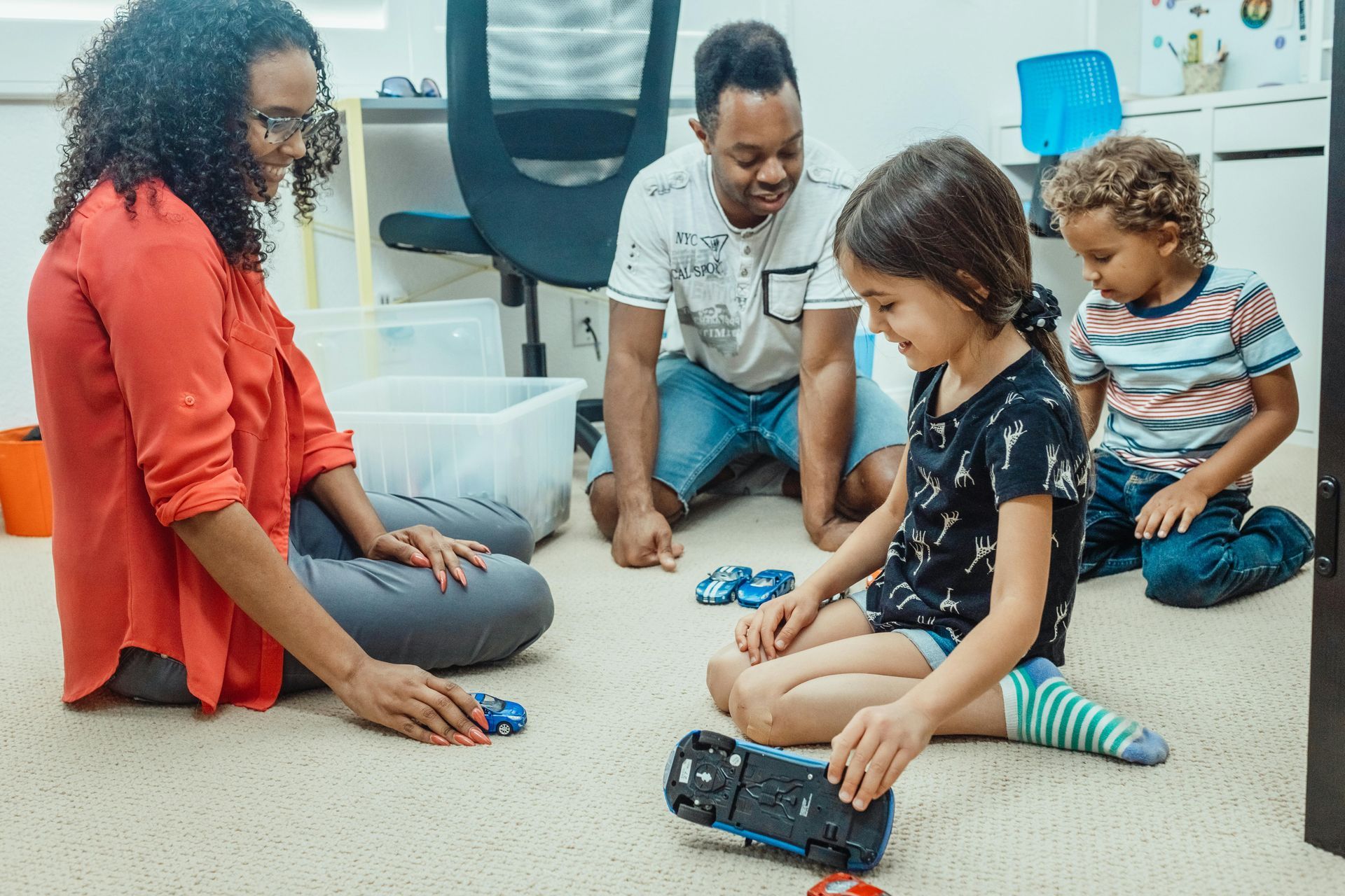 A family is sitting on the floor playing with toys.