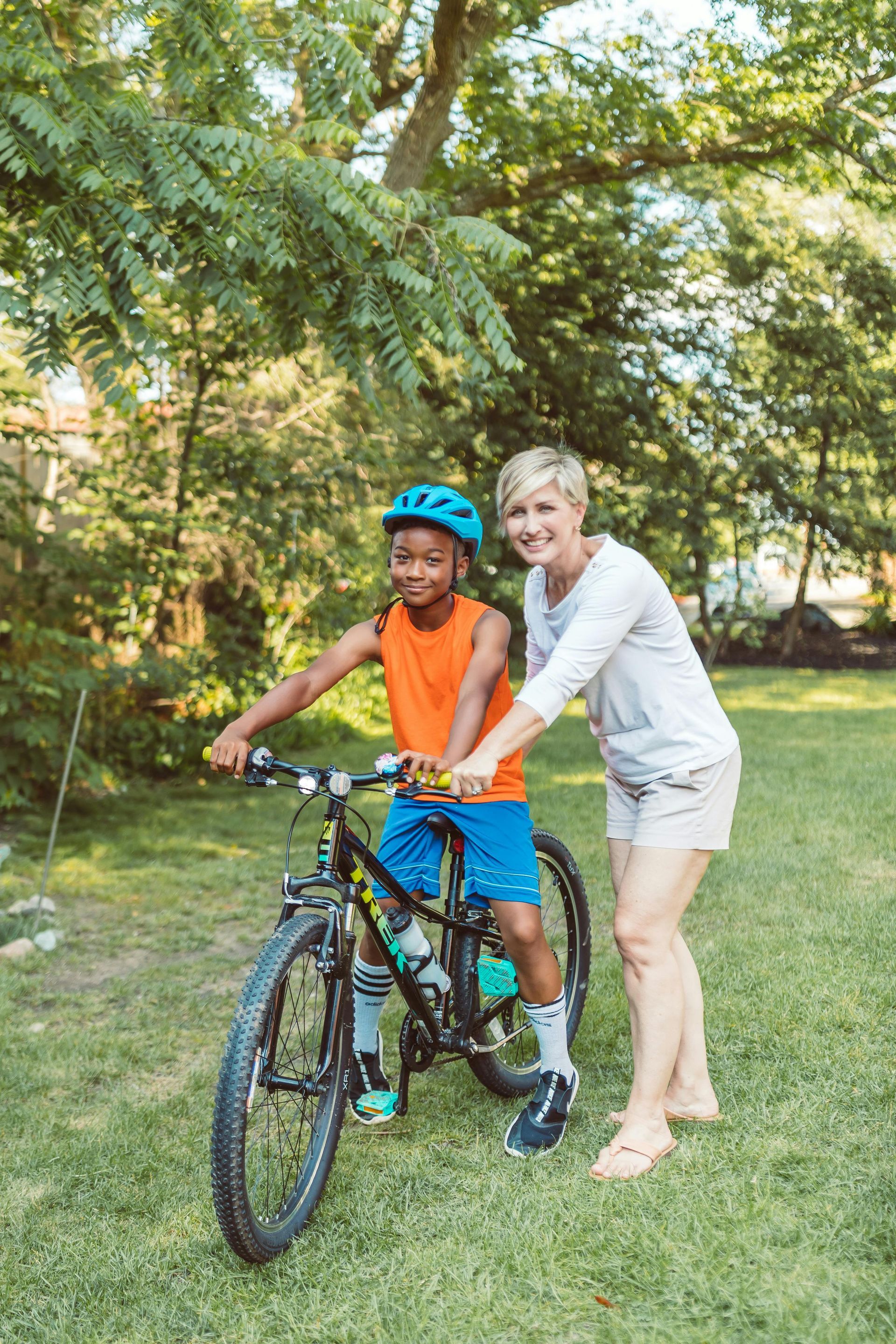A woman is helping a young boy ride a bike in a park.