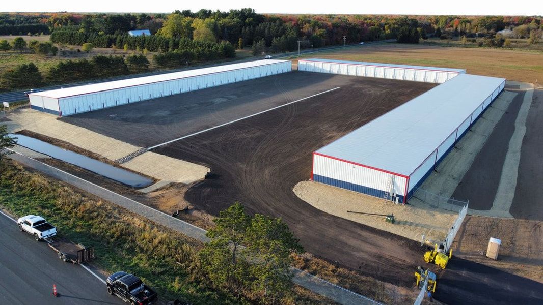 Aerial view of a storage facility with multiple long, white buildings and a gravel parking area.