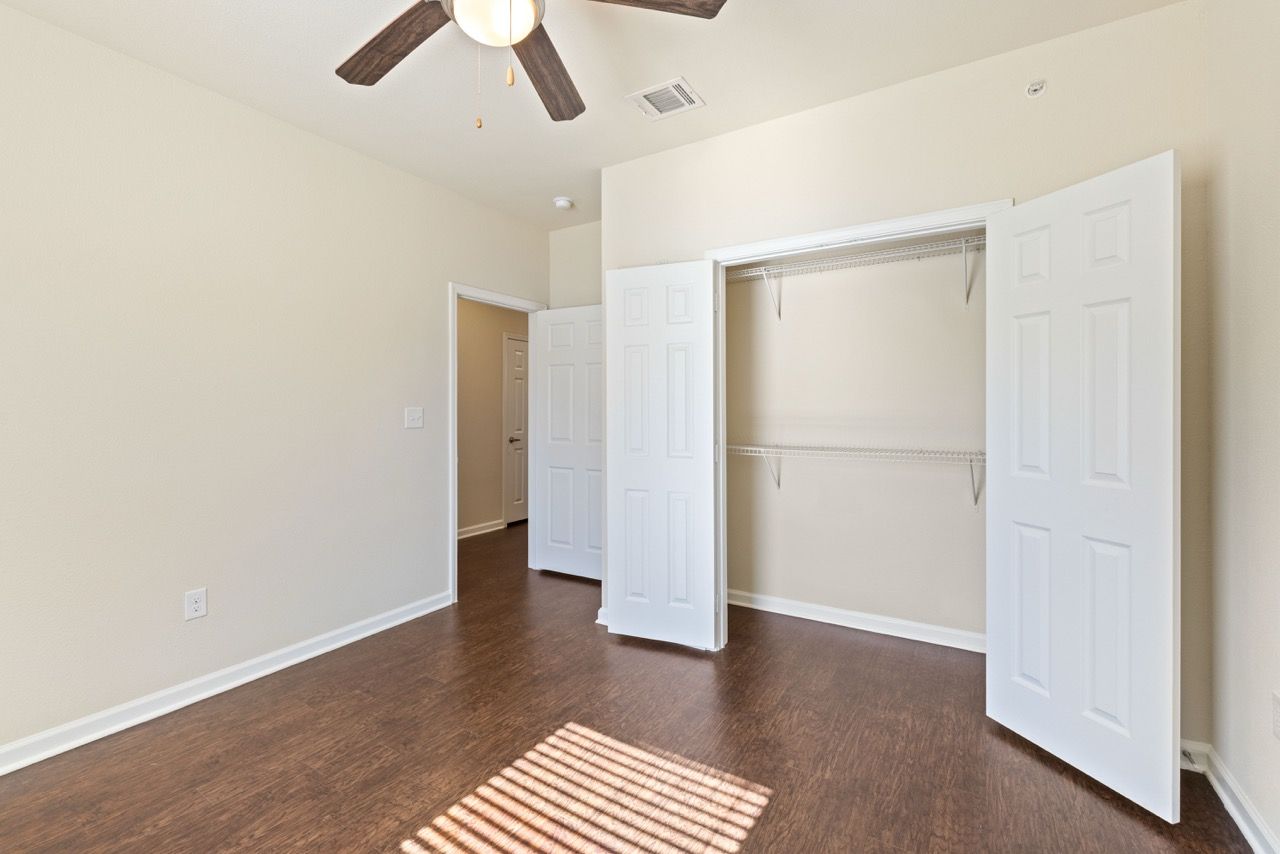 Empty bedroom with wood-style flooring, a white double-door closet with wire shelves, and a ceiling fan.
