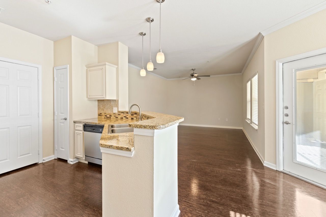 Open-concept kitchen with granite island, stainless steel appliances, pendant lights, and living area.