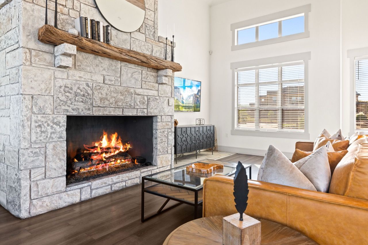 Living room with stone fireplace, large windows, and tan leather sofa.