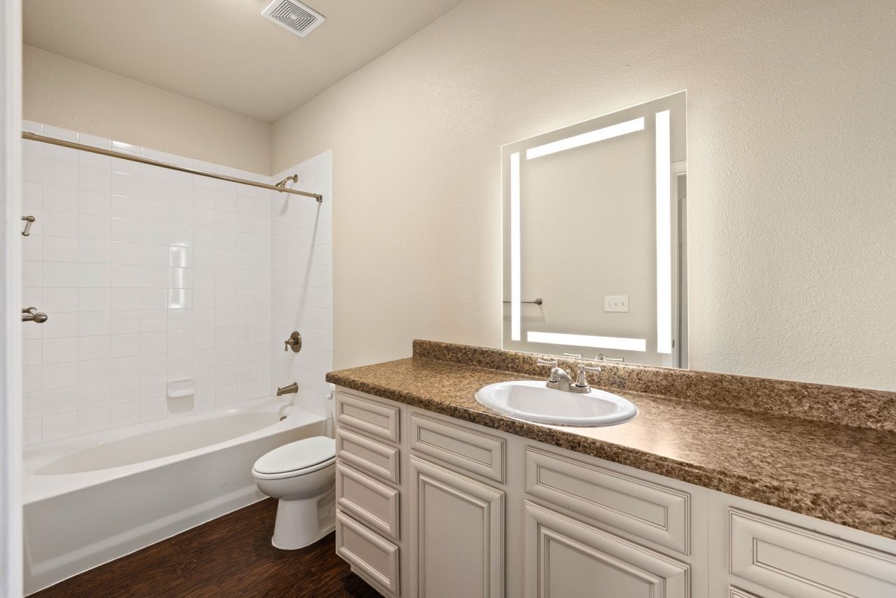 Apartment bathroom with a brown granite vanity, sink, toilet, and white-tiled tub/shower.