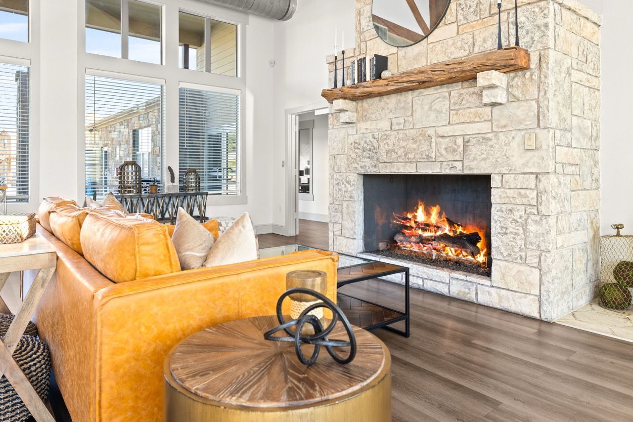 Bright living room with a stone fireplace, orange sofa, glass coffee table, and large windows.