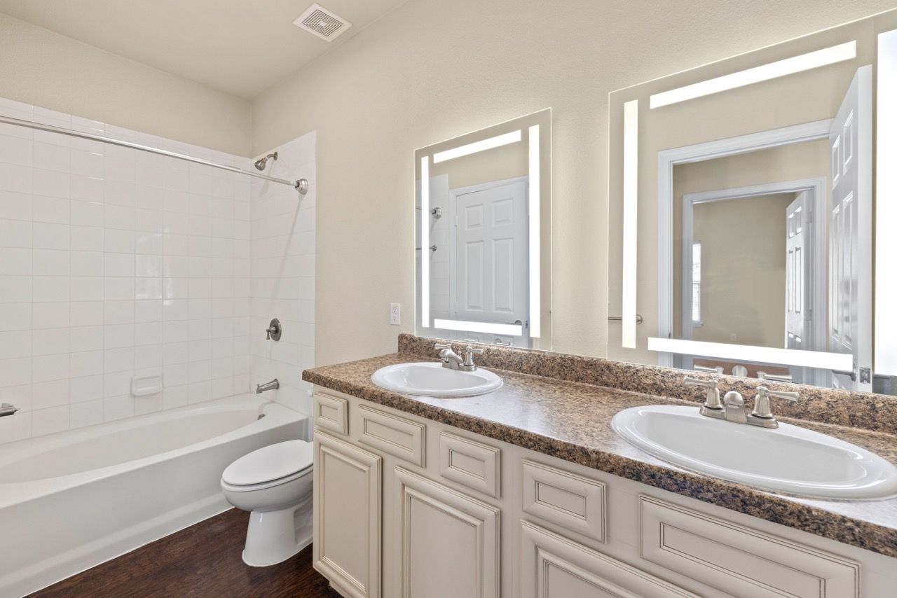 Bathroom with double-sink vanity, granite countertop, and a bathtub/shower combo.