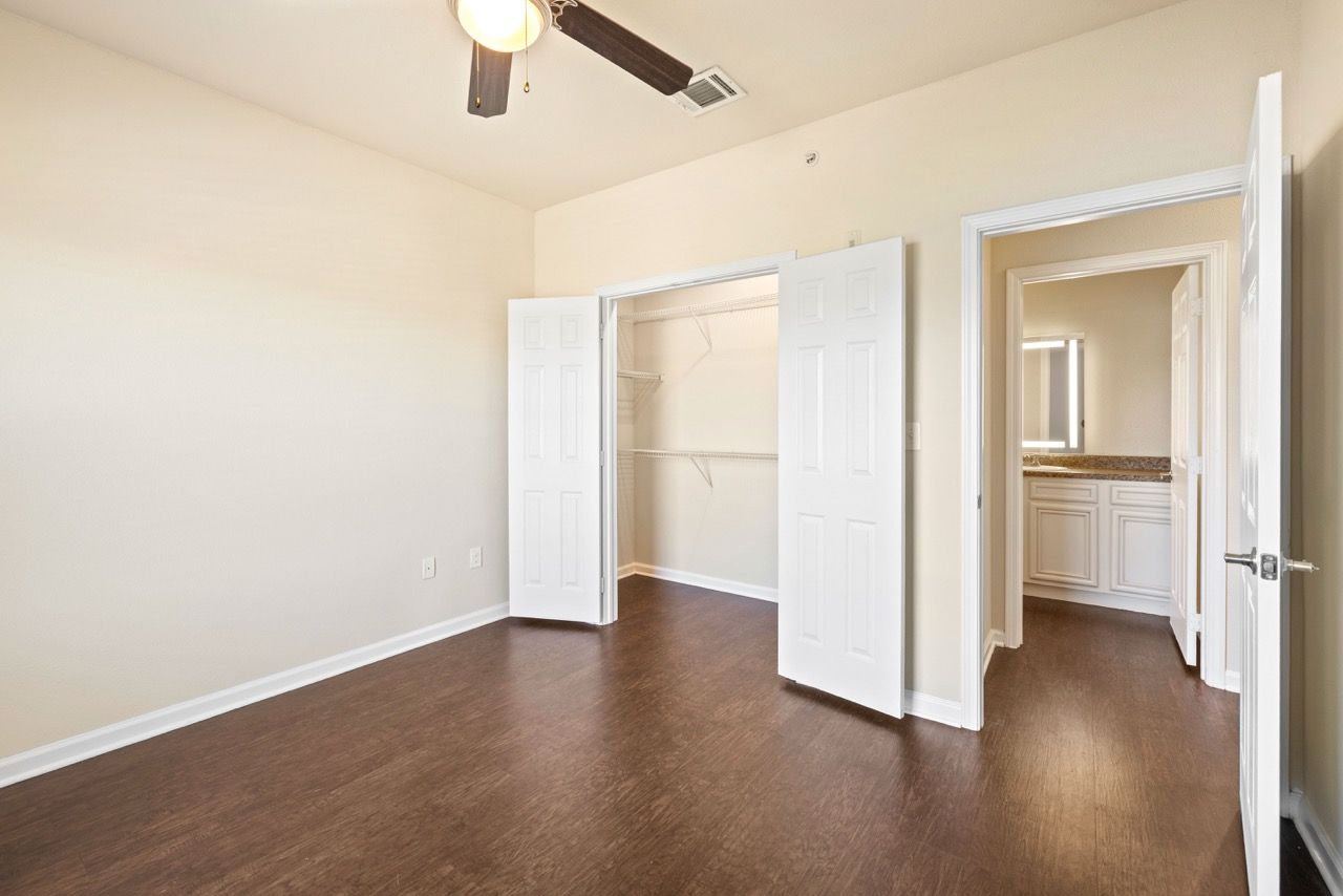Bedroom with wood-style flooring, open double closet doors, and a doorway to the bathroom.