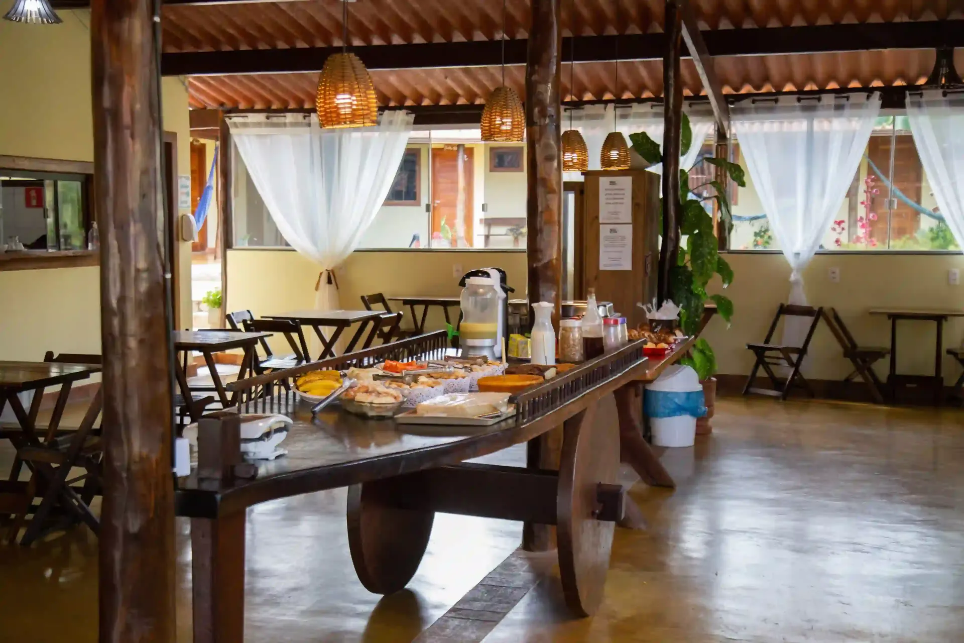 Há uma longa mesa de madeira no meio da sala. pousada-dos-guias