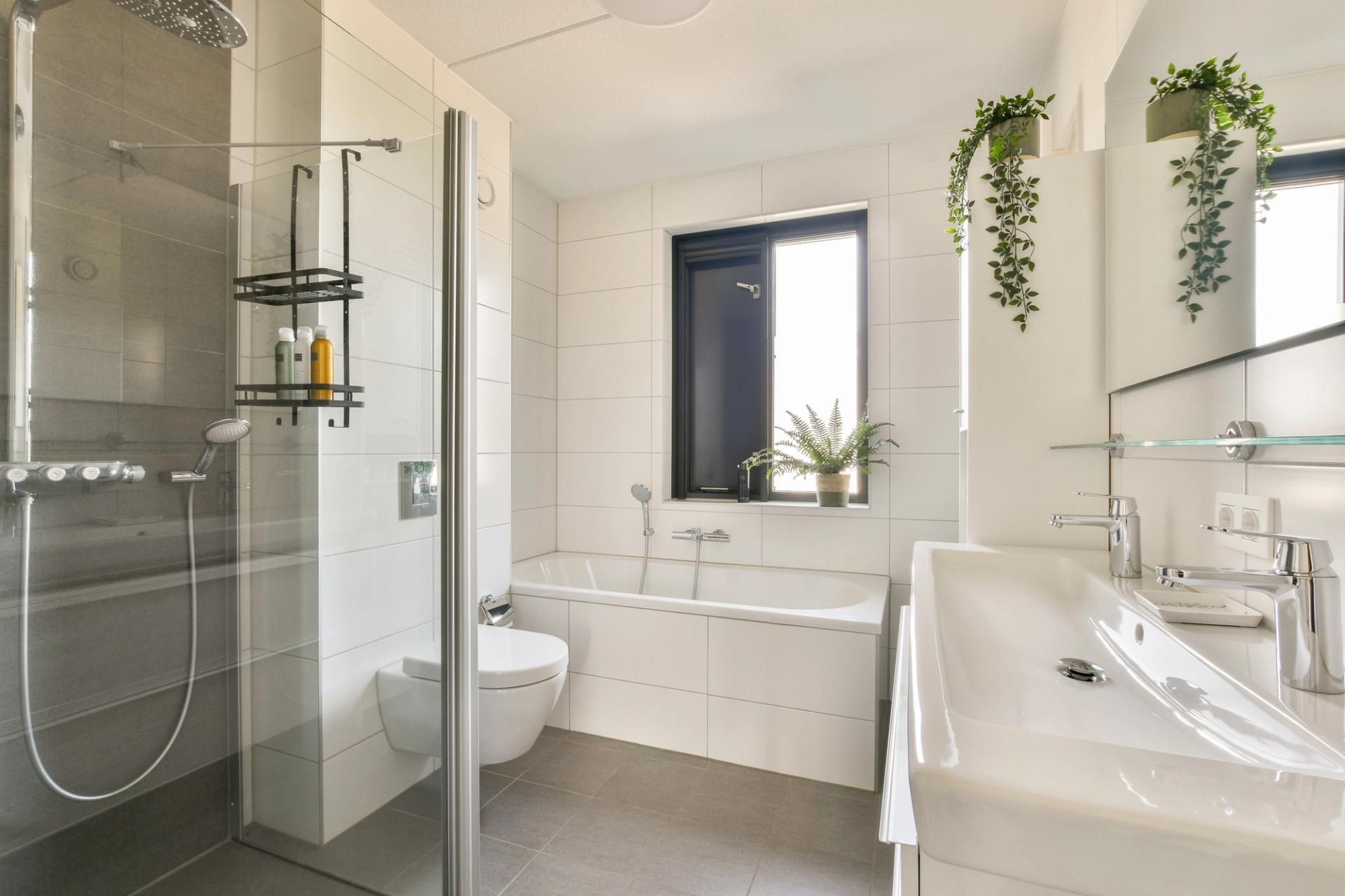 Moderno bagno bianco con doccia, vasca, WC e lavandino, caratterizzato da una piccola finestra e piante sospese.