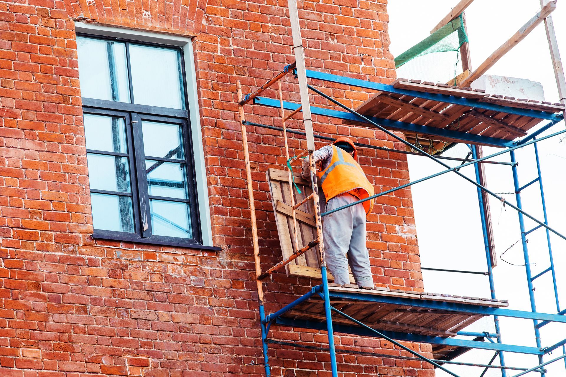 A man is standing on a scaffolding on the side of a brick building.