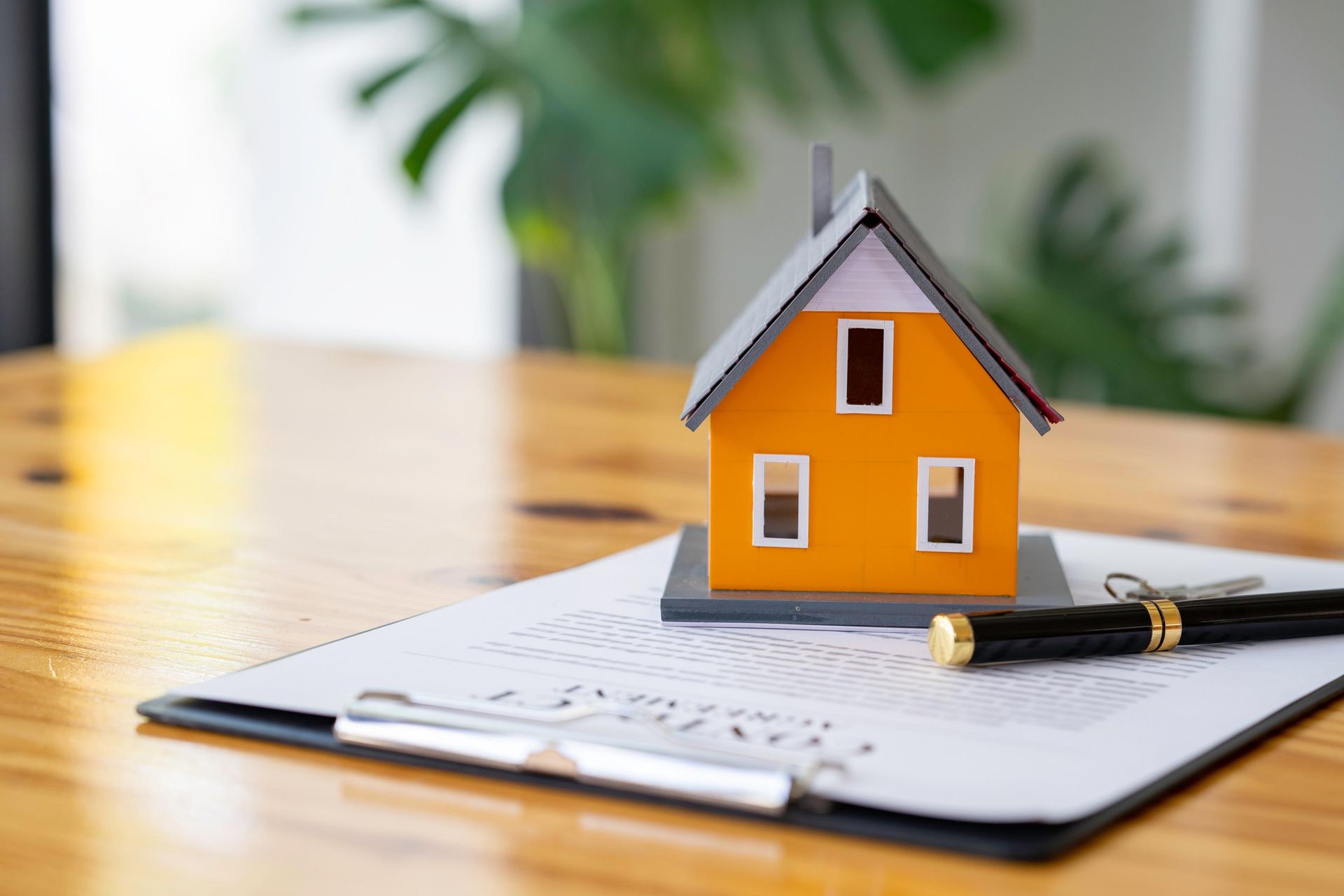 Model house on contract with pen and keys on wooden table, plant background.