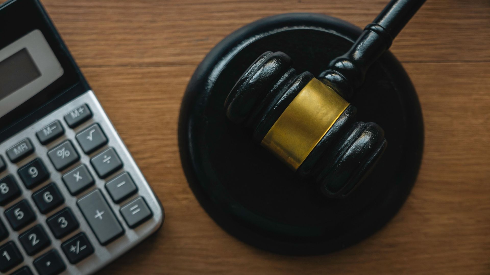 Calculator next to a gavel and sound block on a wooden surface.