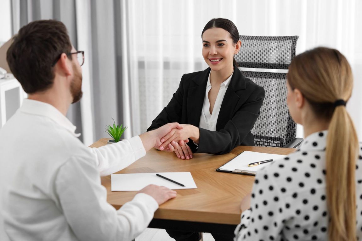 Woman in blazer shaking hands with a man at a table, smiling.