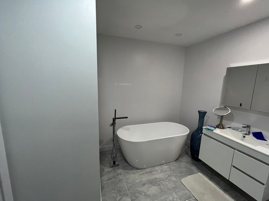 Salle de bains moderne avec baignoire îlot, lavabo et sol carrelé gris.
