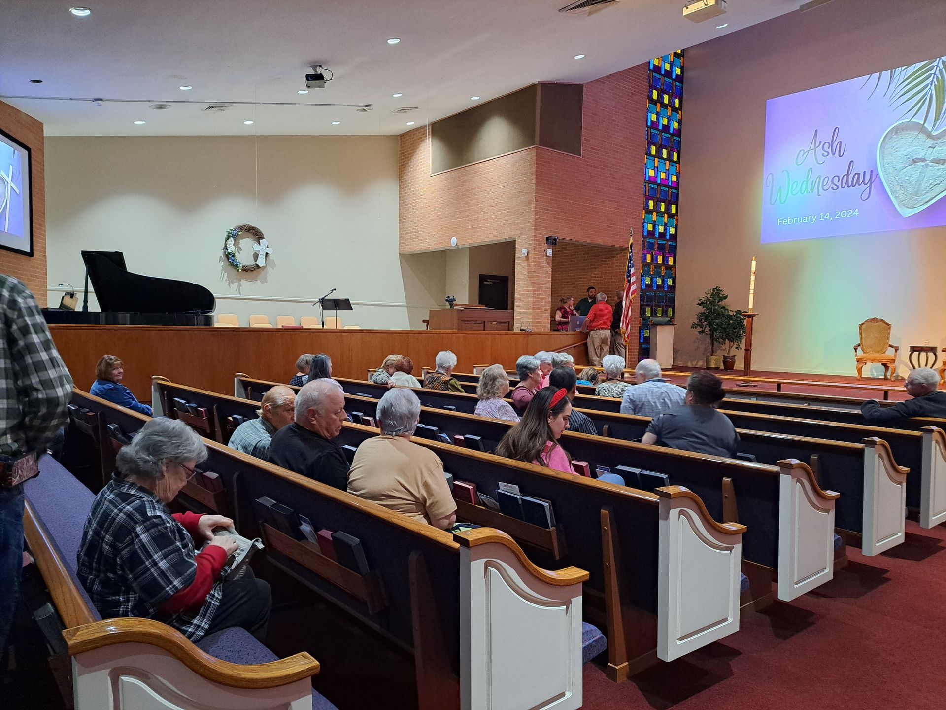 Audience in a church sanctuary, rows of pews, a stage, and a projected image, possibly a presentation.