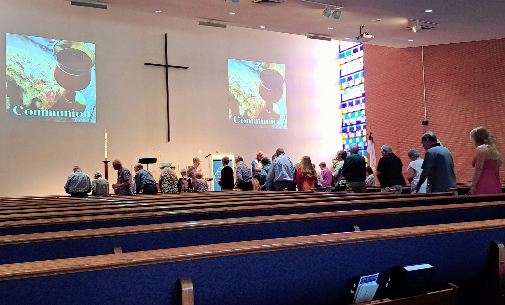 People in a church service, facing a cross, two screens with