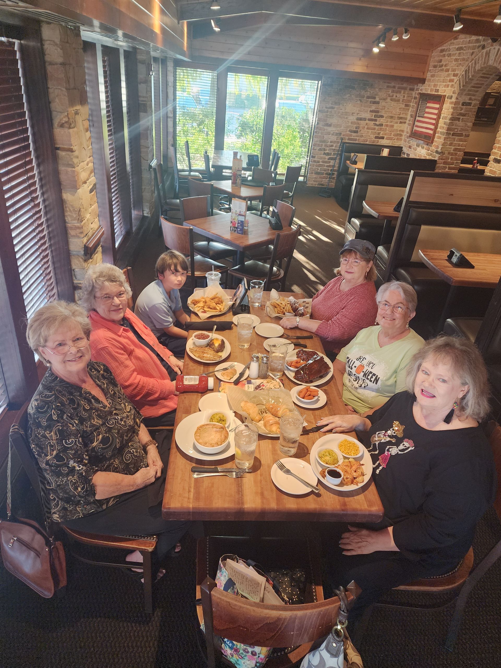 Group of people seated at a restaurant table, enjoying a meal. Sunlight streams through windows.
