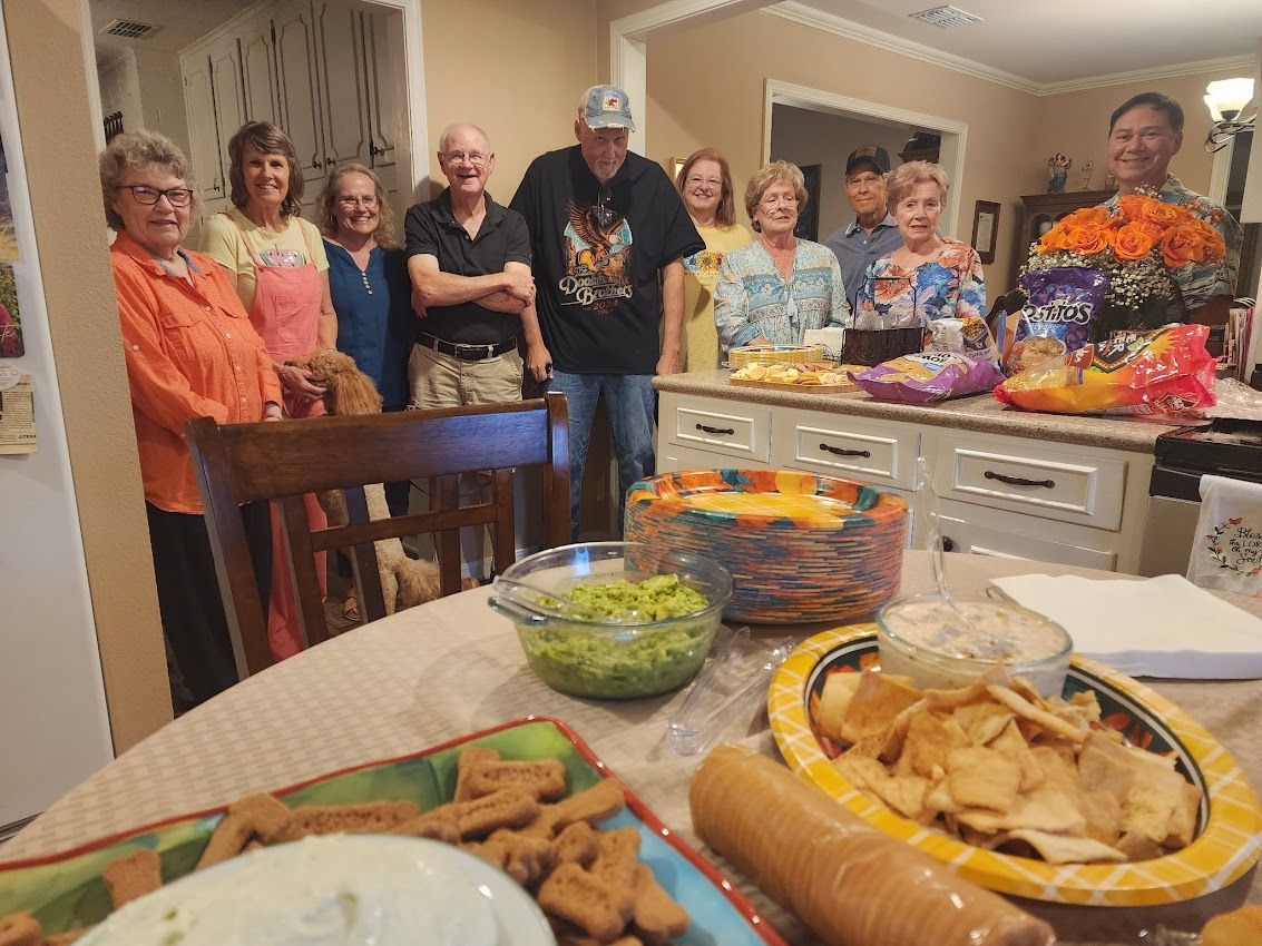 Group of people gathered around a table with snacks, smiling, in a home setting.