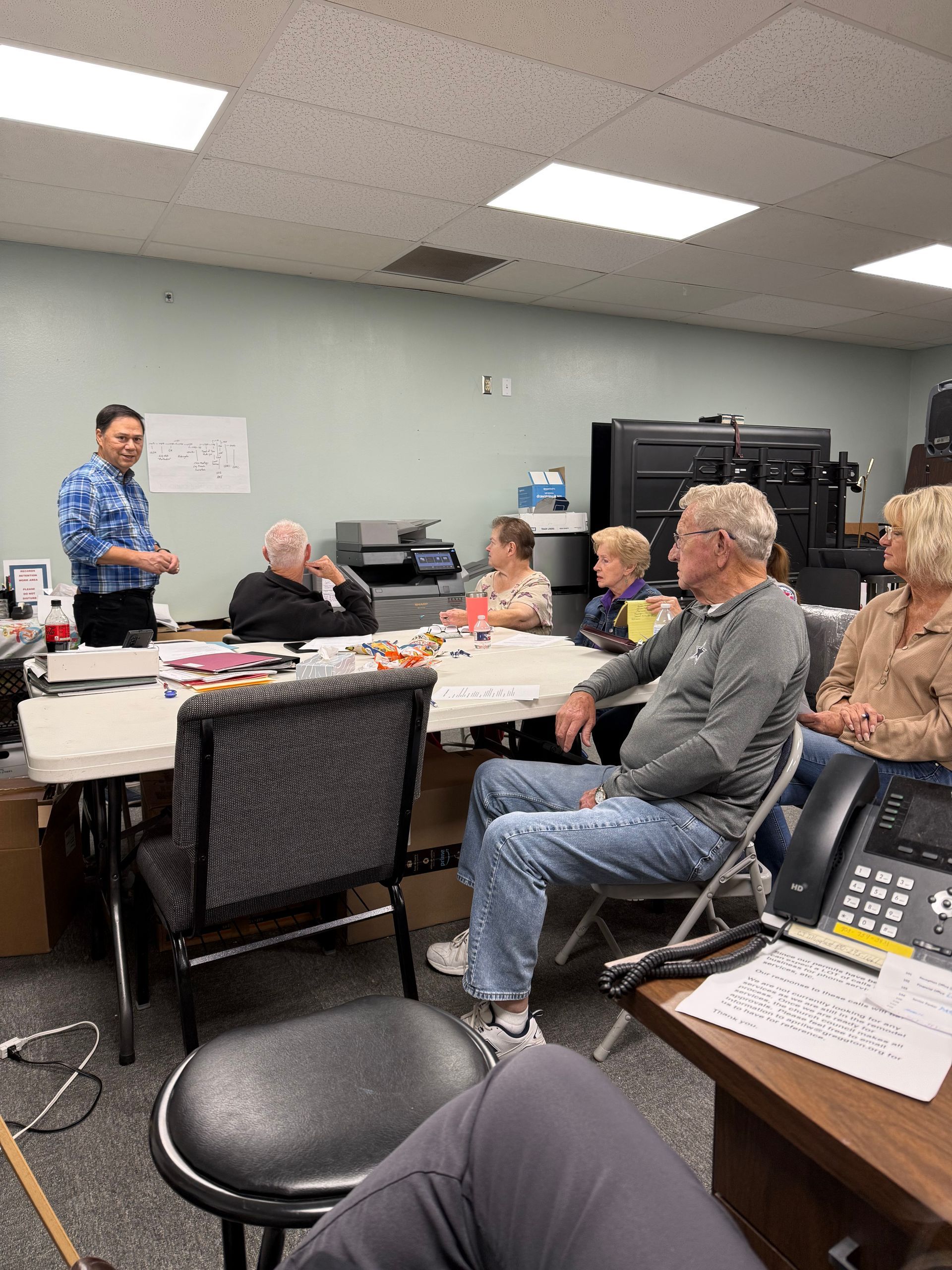 People in a church service; a pastor on the stage, cross on the wall with lyrics projected.
