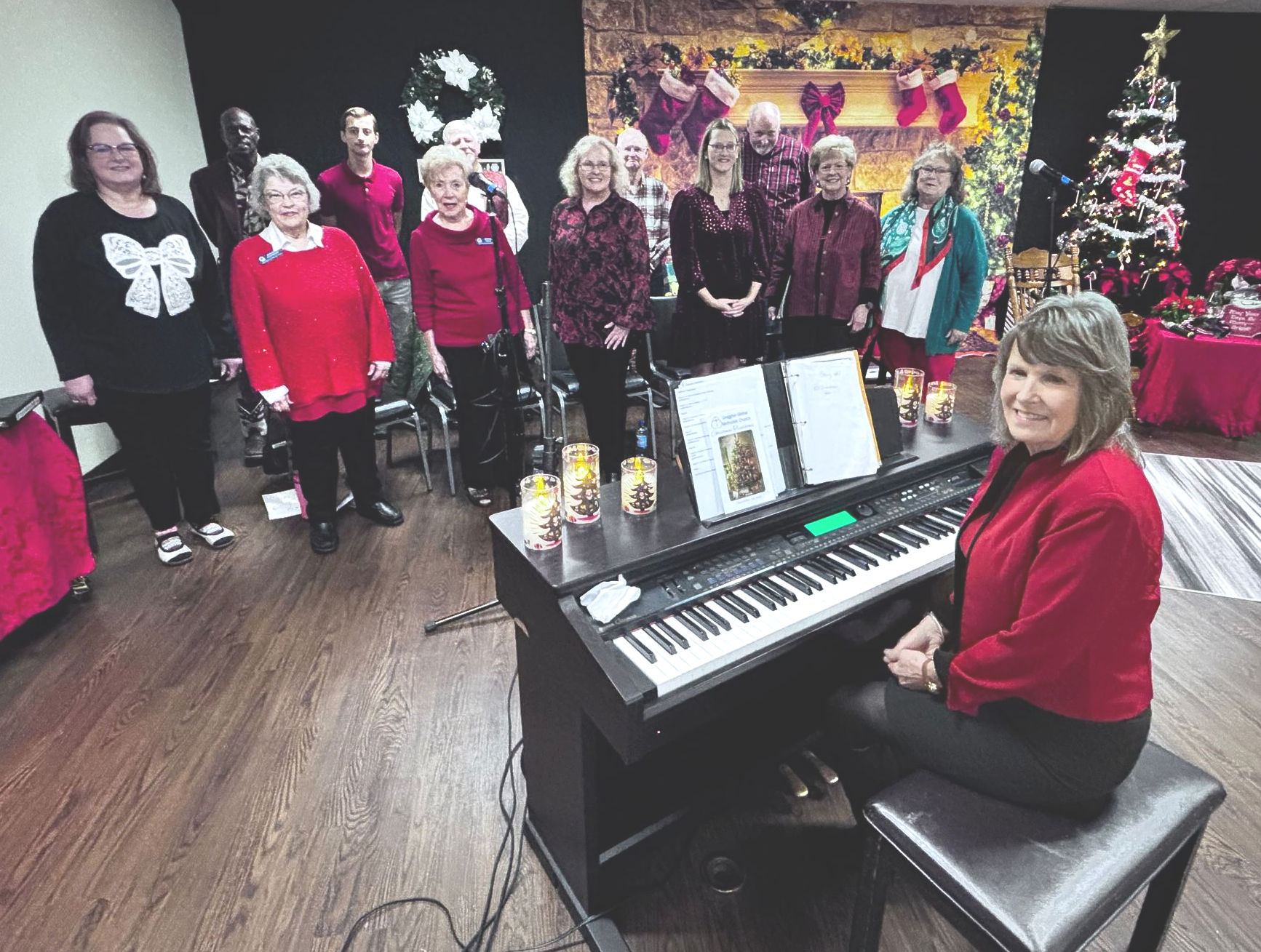 Two people playing guitars and singing into a microphone. One wears a floral top, the other a white dress.