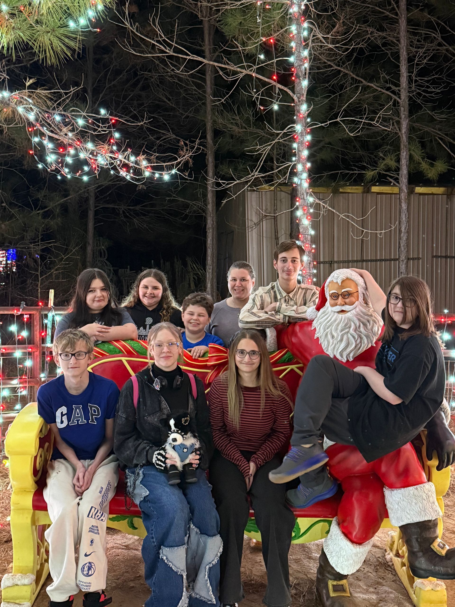 Group of people posing with a Santa statue and holiday lights. Outdoors at night.