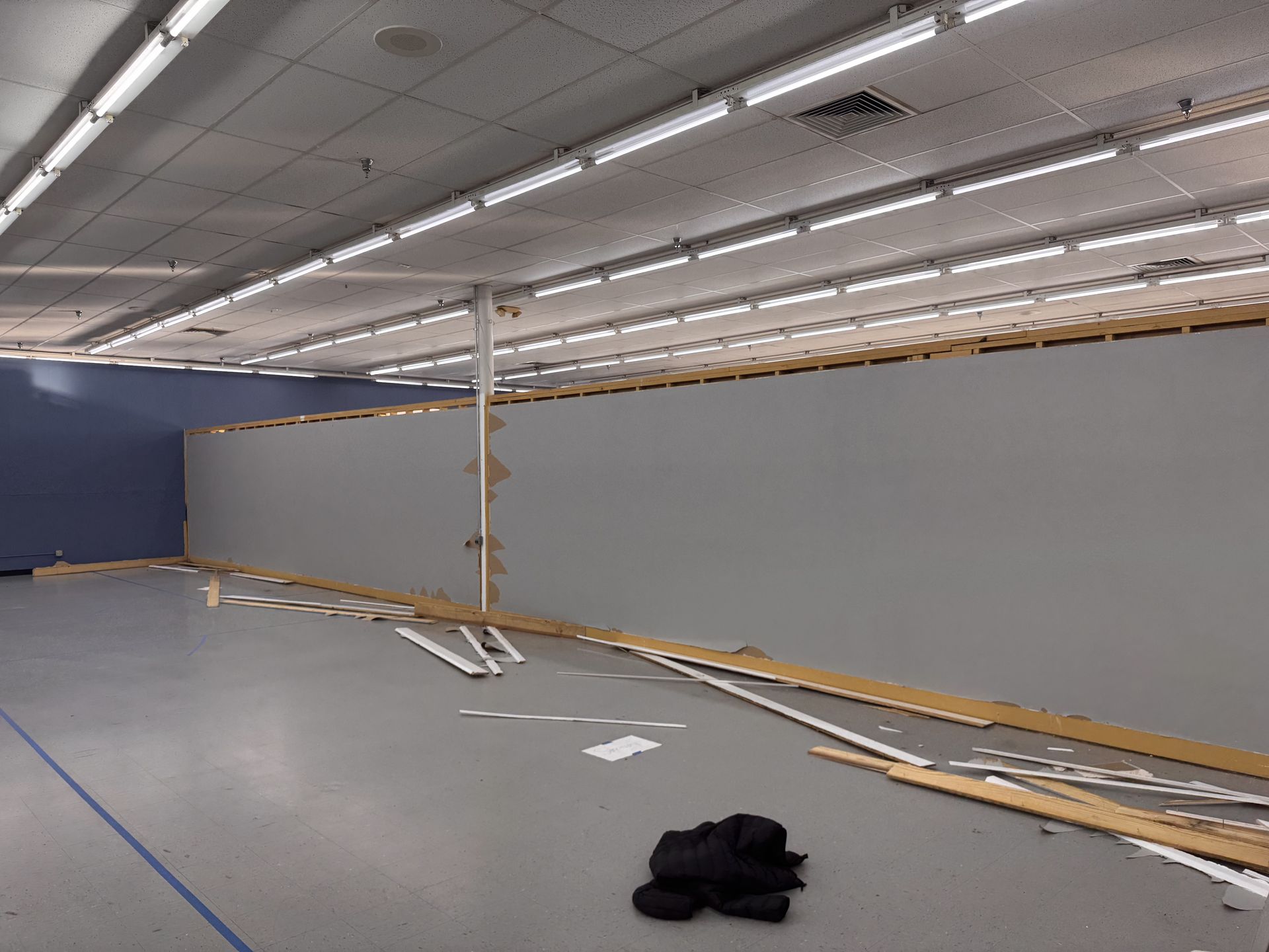 Empty retail space undergoing renovation; gray and blue walls, exposed ceiling, debris on floor.