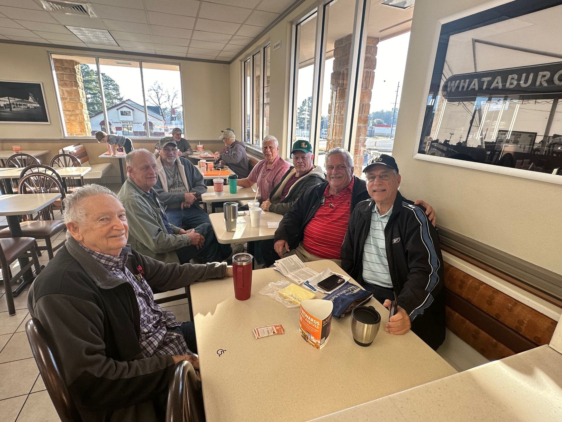 Group of men seated at tables inside a Whataburger restaurant, some smiling and talking.