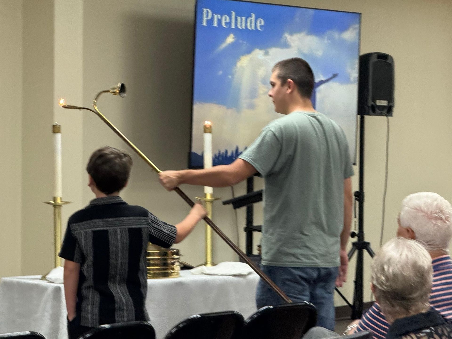 Two people lighting candles at a church altar; a boy and a man with a long candle holder.