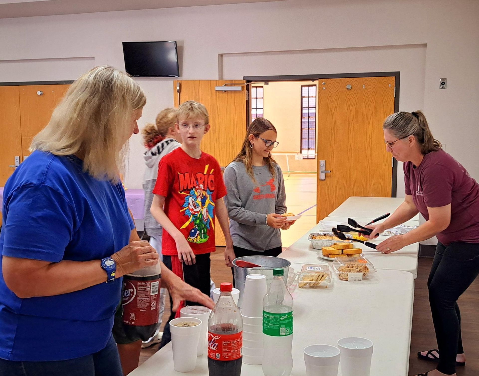 People serving food and drinks at a table in a room.