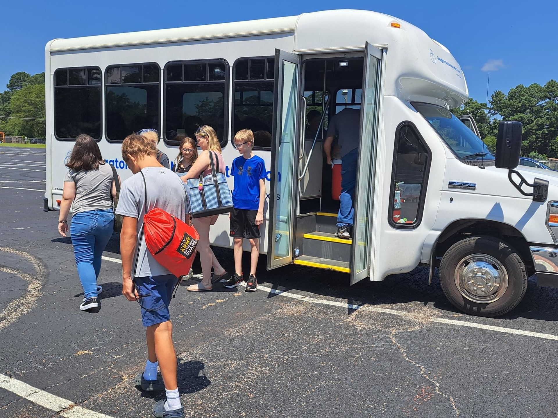 Group of people boarding a white shuttle bus on a sunny day.