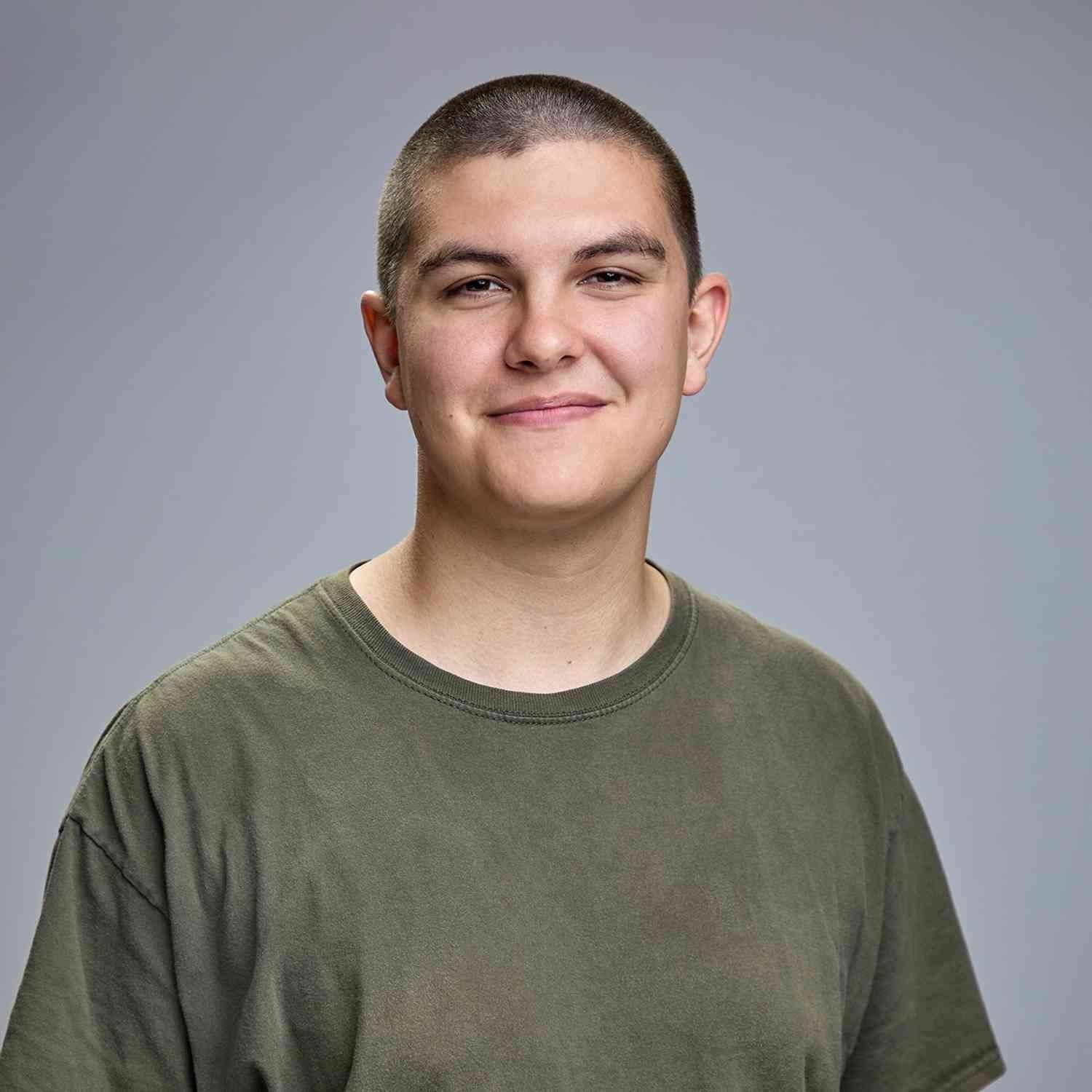 Person with short hair smiles, wearing a green shirt against a gray backdrop.