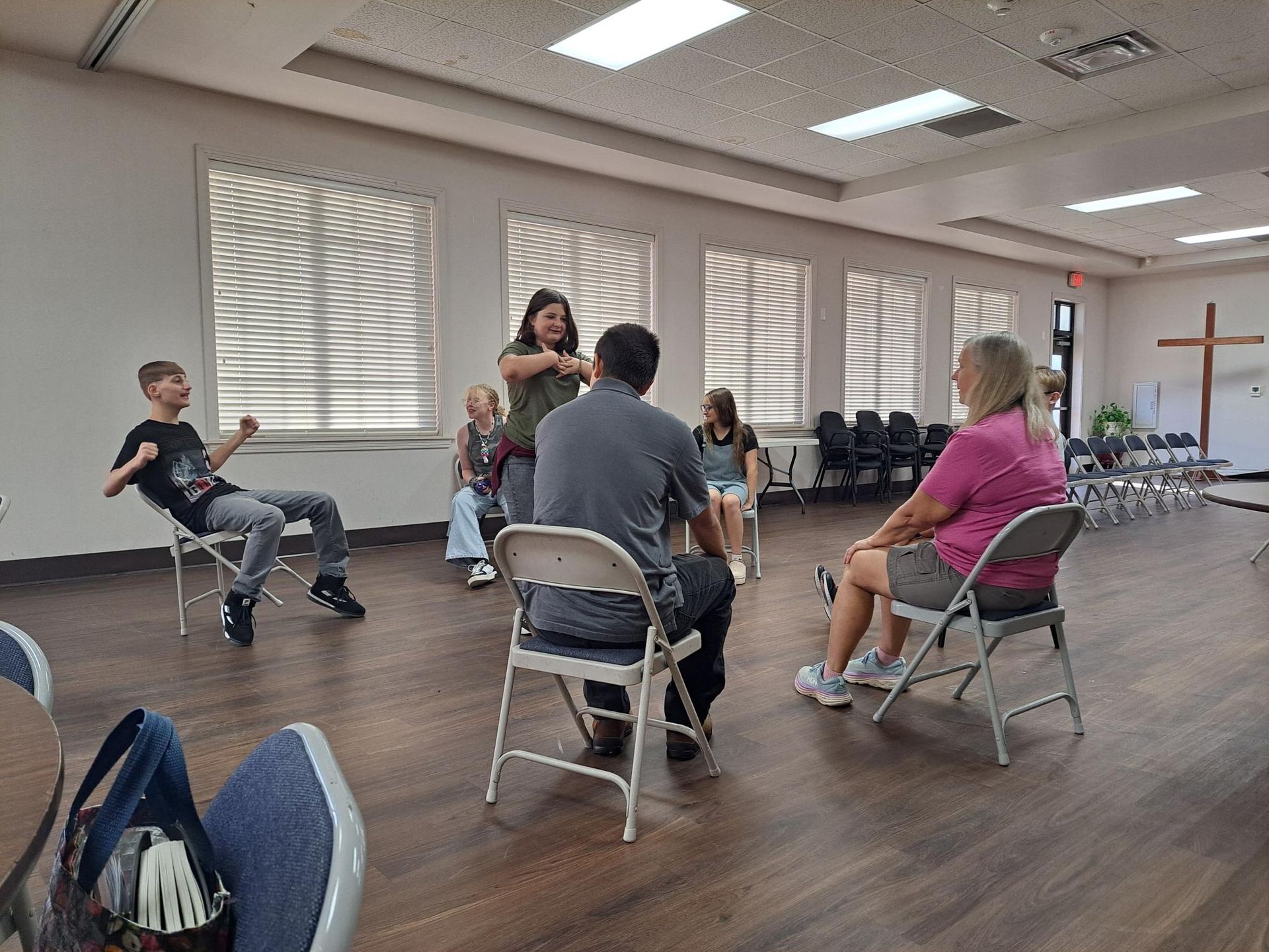 Group of people in chairs, possibly a meeting, in a room with a cross.