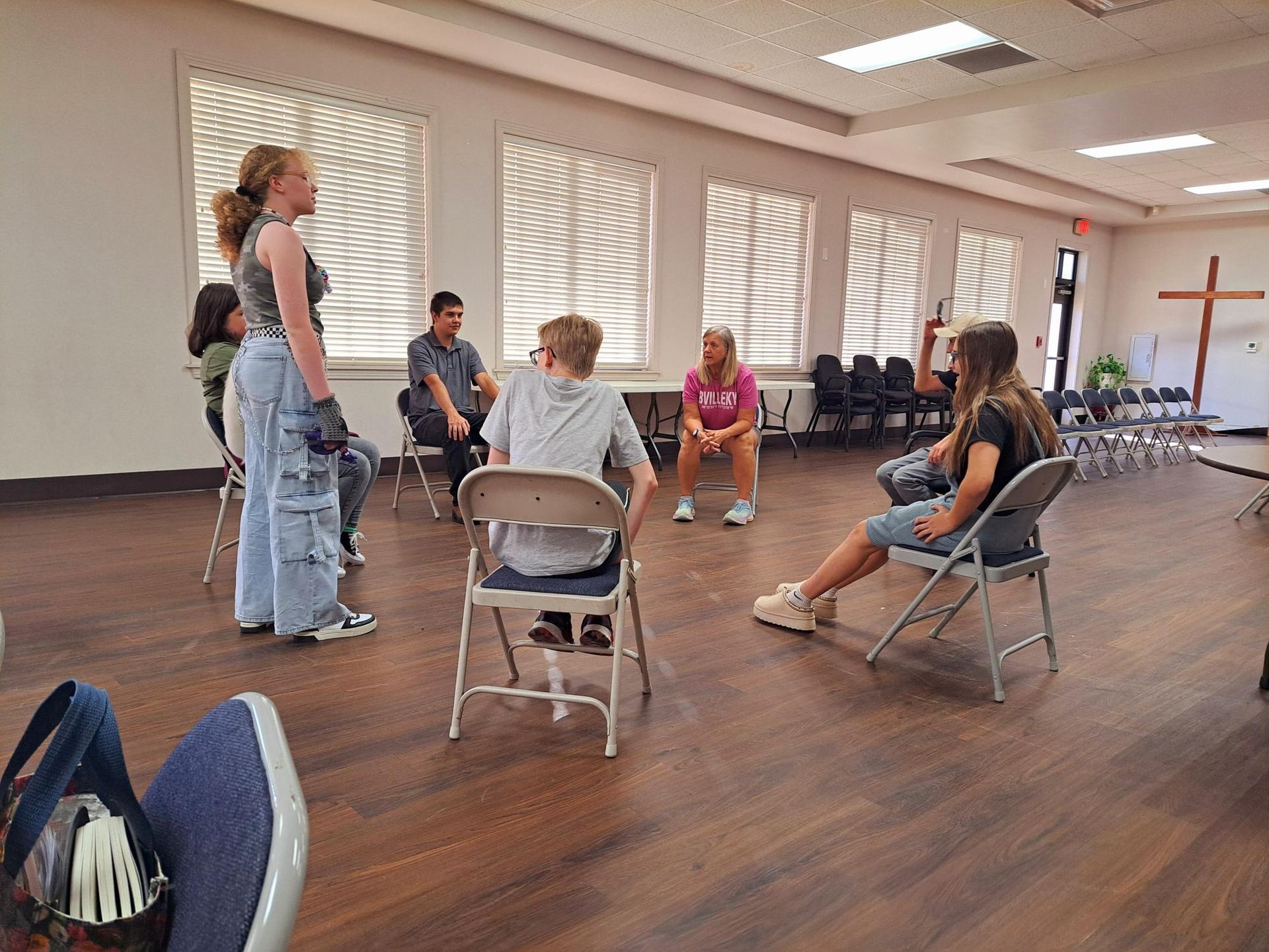 People in a room sit in chairs, some facing each other. There is a young person speaking.