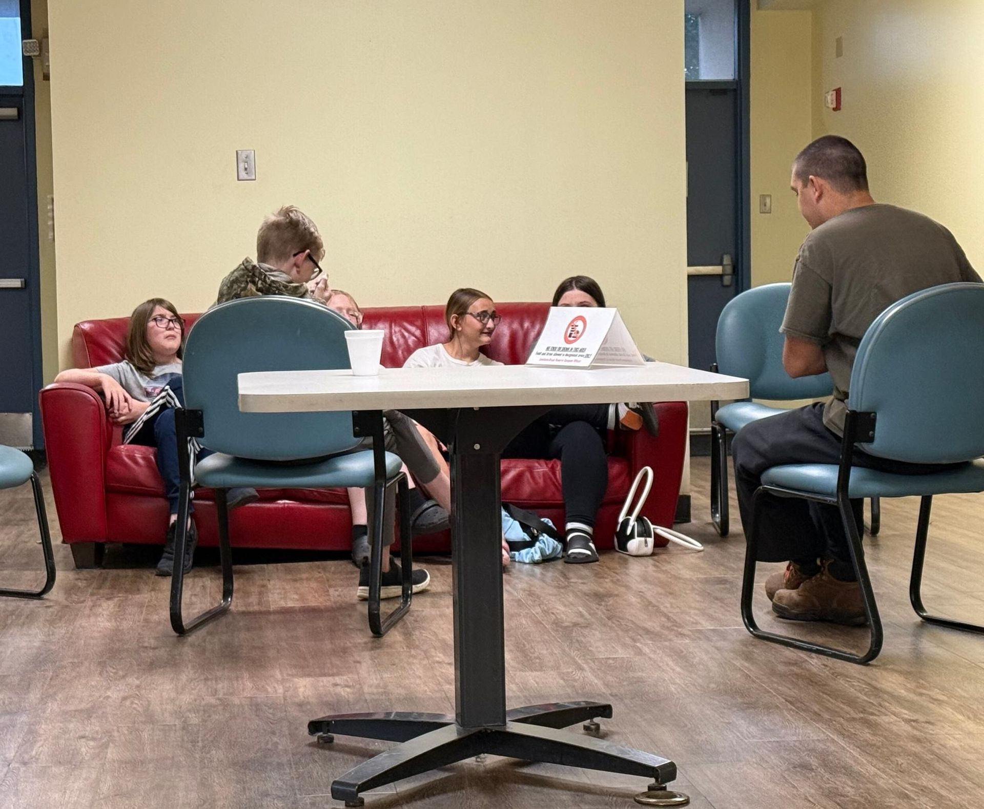 People seated at a table and on a red couch in a room with blue chairs.