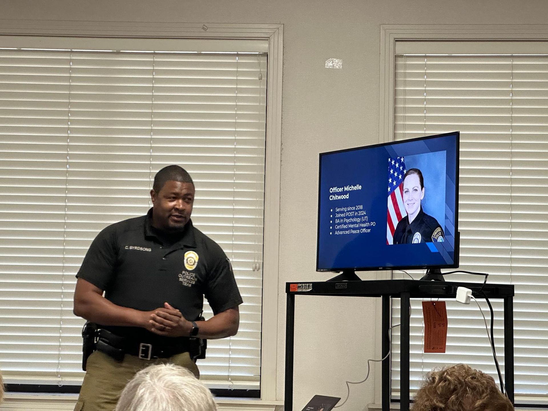 Police officer giving a presentation in a room, with a screen showing information.