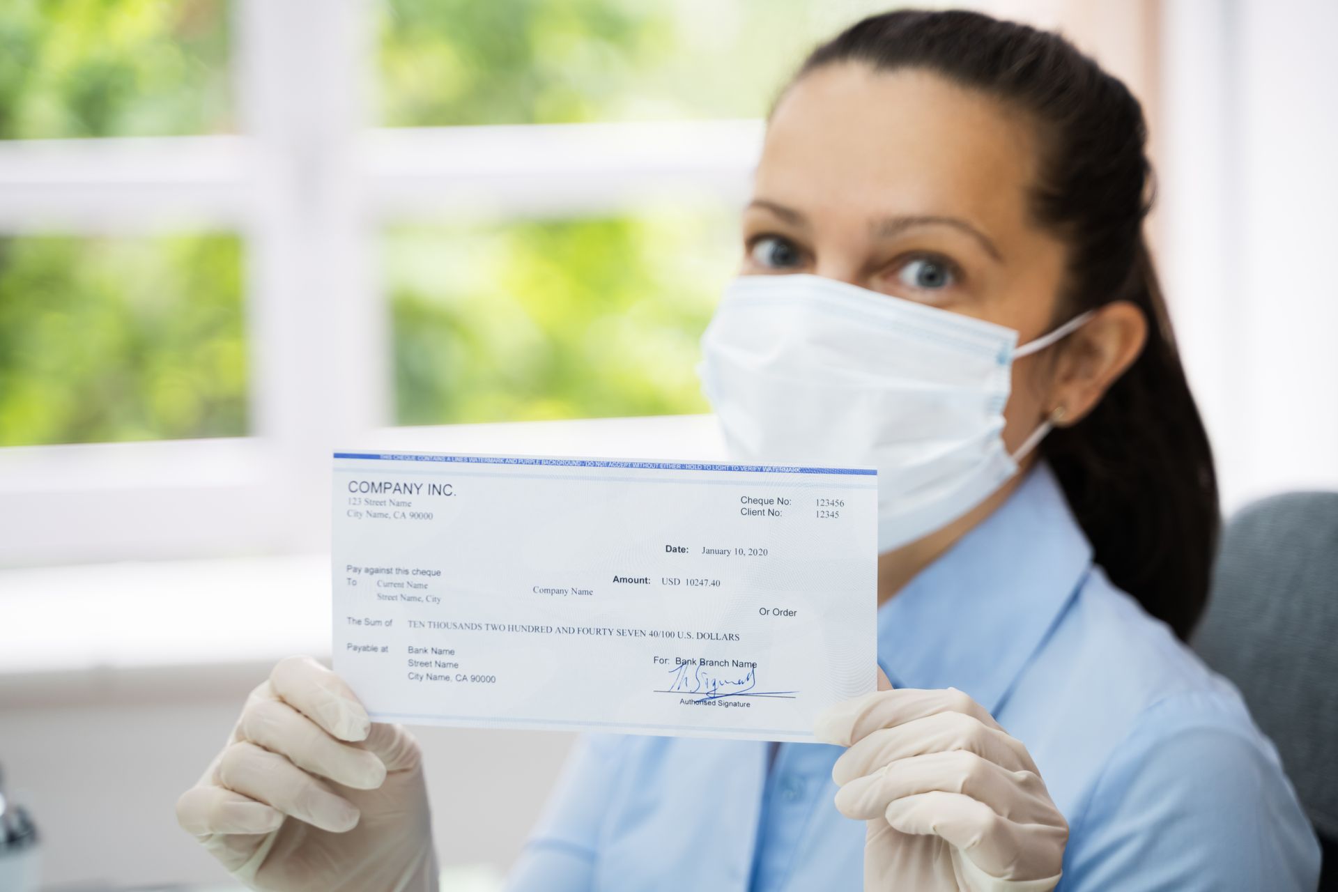 Woman in face mask holding paycheck.