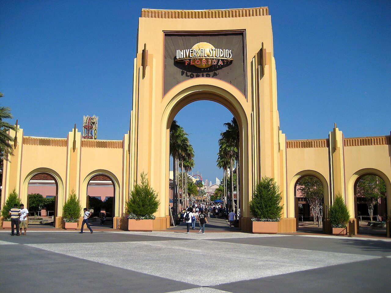 Universal Studios entrance arch with palm trees and people walking under a blue sky