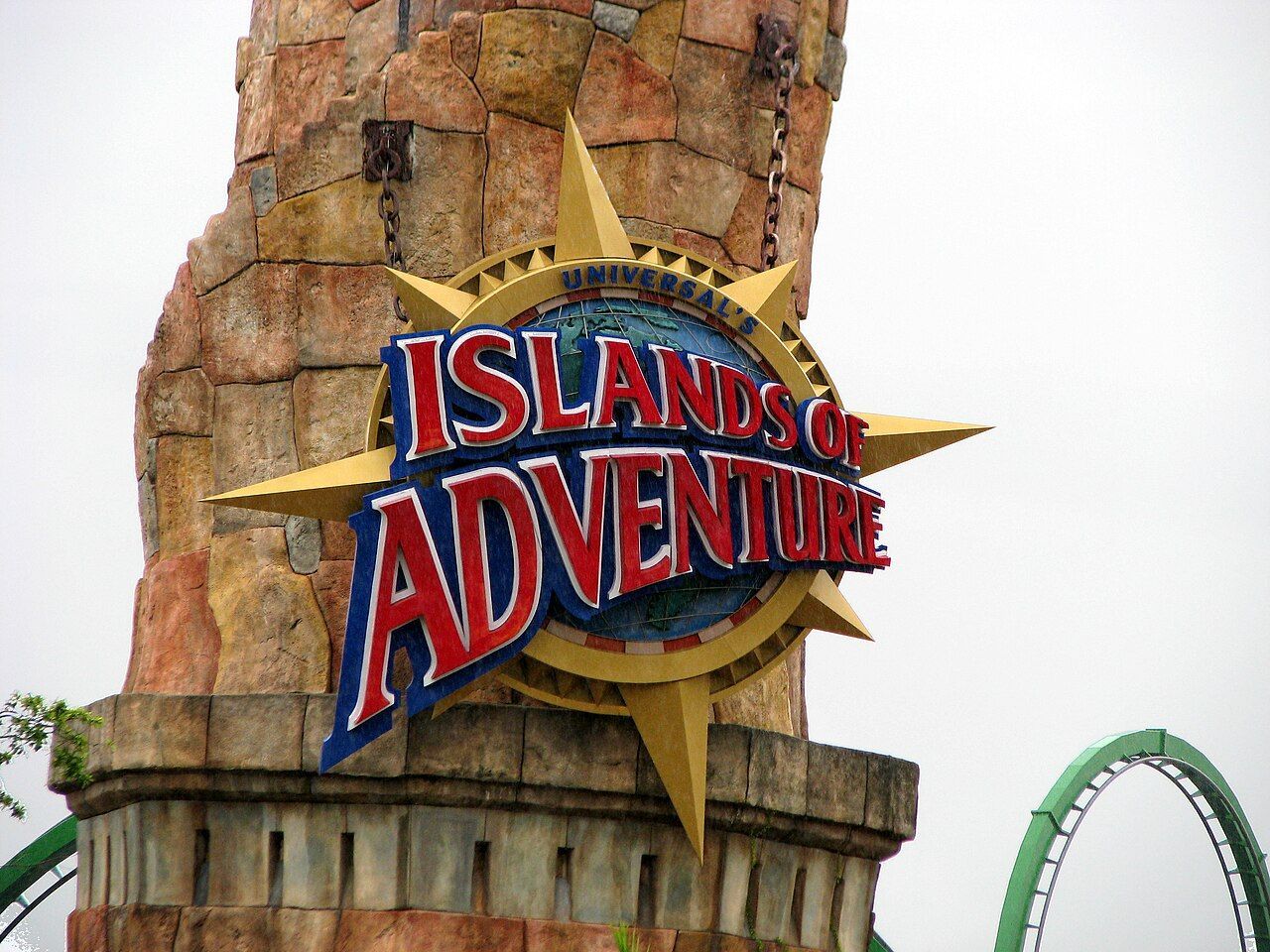 Islands of Adventure sign on a stone tower, with a roller coaster track in the background