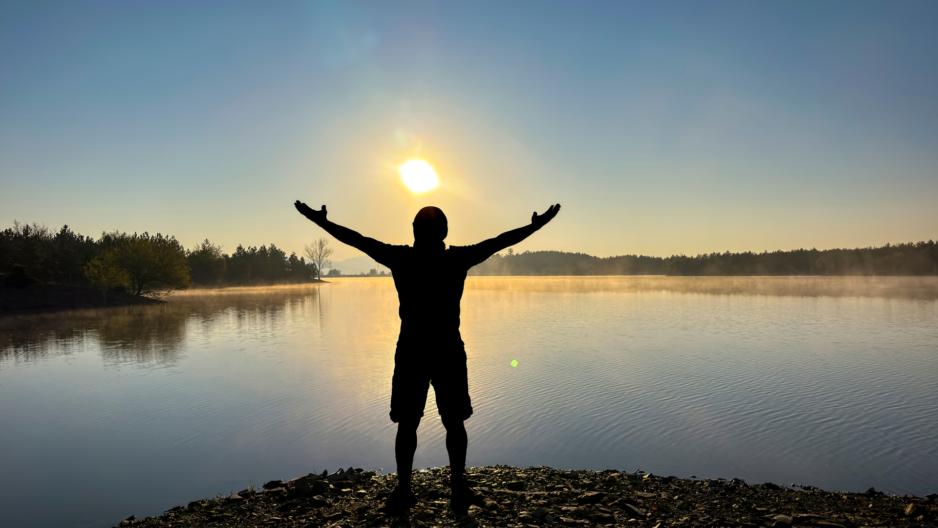 Person with arms raised in front of a sunrise.