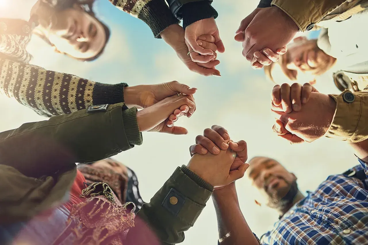 A group of people joining hands in a circle, representing community engagement.